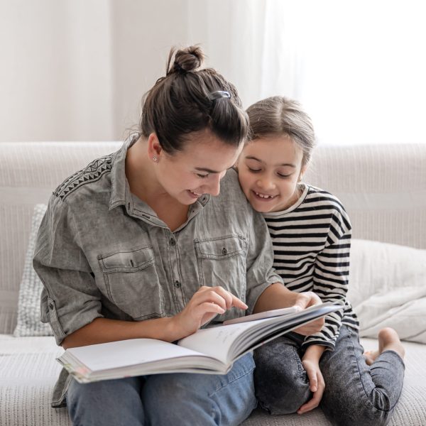 Cheerful mom and daughter are resting at home, reading a book together. The concept of a happy family and friendly relations.